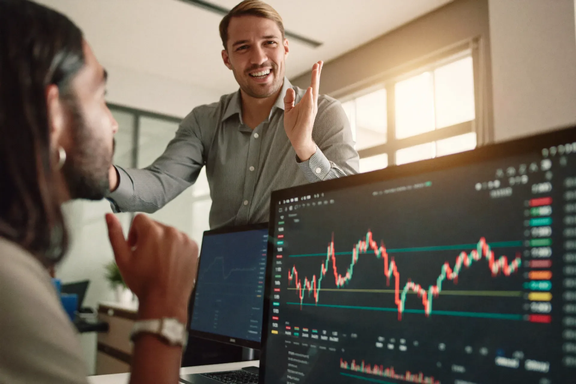 Colleagues celebrating a successful deal in front of a trading screen